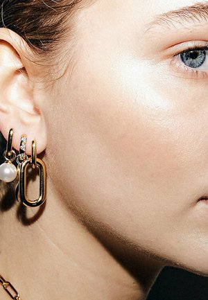 Gold hoop earrings featuring a large oval link, a small pearl, and a section adorned with clear rhinestones. Smooth, metallic texture.