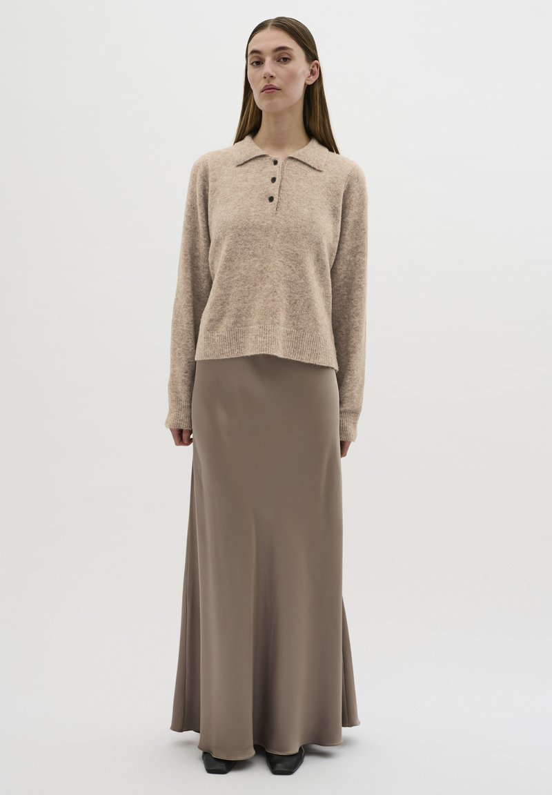 Beige, stickad tröja med krage och tre knappar, i kombination med en slät, lång brun kjol. Outfiten har en avslappnad passform och subtil textur.