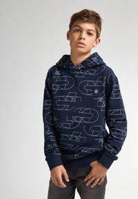 Sudadera azul marino hecha de tela suave, con patrones geométricos blancos. Tiene capucha con cordón y puños acanalados, además de un bolsillo en la parte frontal.