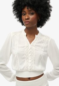 Witte blouse met een mandarinnekraag, kantdetails en knopen aan de voorkant. Gemaakt van een lichte stof met een gestructureerde afwerking.