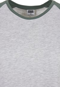 T-shirt gris avec une texture légère et un col côtelé vert. L'étiquette indique "Urban Classics", taille XS, fabriqué au Bangladesh.
