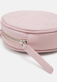 Borsa rotonda in pelle rosa con superficie testurizzata, dotata di chiusura a cerniera e di una piccola tracolla. Design inciso sulla parte superiore.