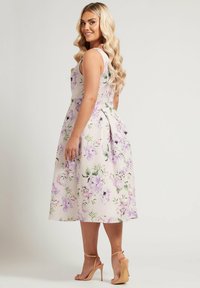 Blommig midi-klänning i ljusrosa med lavendel- och gröna tryck, åtsittande midja, breda axelremmar och en flödande kjol med sidofickor.