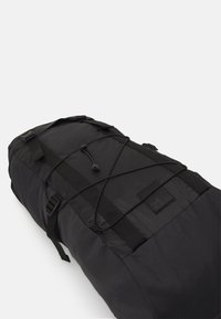 Crni dukserica s teksturiranom tkaninom, podesivim trakama i elastičnom detaljnom žicom. Ima pravokutni oblik i tonalne brendirane oznake.