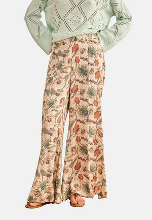Pantalones de pierna ancha con un estampado floral en tonos apagados combinados con un suéter de punto verde claro con textura y sandalias.