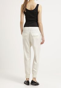Pantalons de jogging blancs, ajustés avec une taille élastique et des poignets. Ils disposent de poches arrière et d'un tissu lisse et léger.