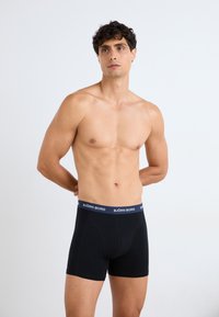 Schwarze Boxershorts aus glattem Stoff mit einem marineblauen Elastikbund, der das Logo "BJÖRN BORG" trägt. Fitted Design und mittellange Beinlänge.