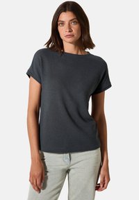 Mørkegrå kortærmet top med et struktureret mønster, rund halsudskæring og afslappet pasform, båret med lyse jeans.