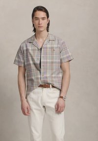 Šortslēga raibā krekls gaisās zilo, zaļo un purpura toņos; aizpogāts ar kempinga apkakli; apvienots ar baltām biksēm un brūnu jostu.