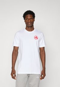 White cotton t-shirt with a round neckline, short sleeves, and a red circular graphic featuring the brand name on the left chest.