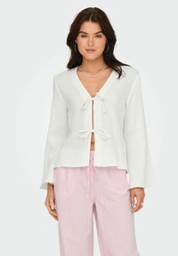 Haut léger blanc à manches longues avec un décolleté en V et deux liens à l'avant. Assorti à un pantalon ample rayé rose clair.