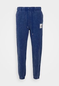 Navyblaue Jogginghosen aus weichem Material, mit einem elastischen Bund, verstellbarem Kordelzug und einem weißen Logo-Patch am linken Oberschenkel.