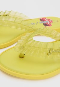 Sandales en caoutchouc jaunes avec des brides translucides à volants et un motif cerise sur la semelle.