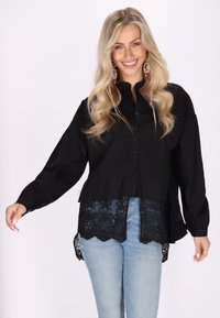 Camicia nera con bottoni, maniche lunghe e dettagli in pizzo all'orlo, abbinata a jeans blu chiaro. Tessuto liscio con una vestibilità comoda.