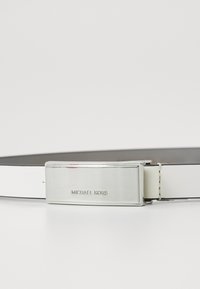 Curea din piele neagră cu o cataramă netedă și lucioasă, de culoare argintie. Catarama are gravată textul "MICHAEL KORS" și are o formă rectangulară.
