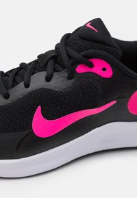 Melnas sporta kurpes ar tīkla augšdaļu, rozā akcentiem, izteiksmīgu swoosh simbolu un baltu zoli. Iezīmes auklas un teksturētas virsmas detaļas.