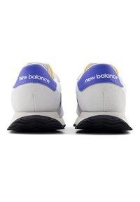 Bílé a šedé tenisky s fialovými detaily, s texturovaným semišovým povrchem, gumovou podrážkou a logem "new balance" na patě.