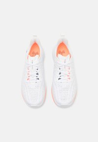 Chaussures de sport blanches avec une tige en mesh respirant, doublure intérieure orange, lacets blancs et accents de logo noirs contrastants sur les côtés.