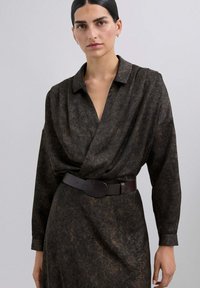 Vestido marrón con estampado, de mangas largas y cuello con solapa, ceñido en la cintura con un cinturón marrón oscuro que tiene una hebilla redonda.