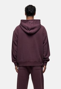 Haut à capuche bordeaux avec cordon de serrage, coupe ample, poignets et ourlet côtelés. Associé à un pantalon assorti avec poches latérales. Texture de tissu doux.