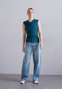 Tyrkfarget ermeløs topp med drapert utringning, kombinert med lyseblå vid bukse og hvite slip-on sko. Glatt stoff og avslappet passform.