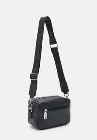 Black leather crossbody bag with silver hardware, zippered compartments, and an adjustable strap featuring embossed brand name.