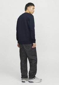 Marineblauwe sweatshirt met een ronde halslijn, ribgebreide boorden en tailleband. Gecombineerd met donkere spijkerbroek en lichtgrijze sneakers met zwarte accenten.