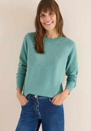 Suéter de cuello redondo en un suave tejido de punto en tono azul claro, combinado con jeans azules con cierre de botón y bolsillos frontales, mostrando un ajuste relajado.