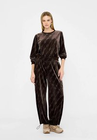 Tuta in velluto marrone con motivo a logo, composta da una maglia a vestibilità rilassata e pantaloni affusolati. Il design include una vita con coulisse e polsini.