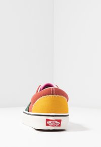 Wielokolorowy sneaker na płóciennej podeszwie z pomarańczowymi, żółtymi, zielonymi i różowymi panelami; posiada białą podeszwę, czarny pasek oraz czerwoną metkę z logo na pięcie.