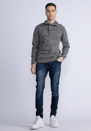 Sweater en tricot gris avec col et détails de boutons, associé à un jean bleu foncé et des baskets blanches. La texture est douce et confortable.