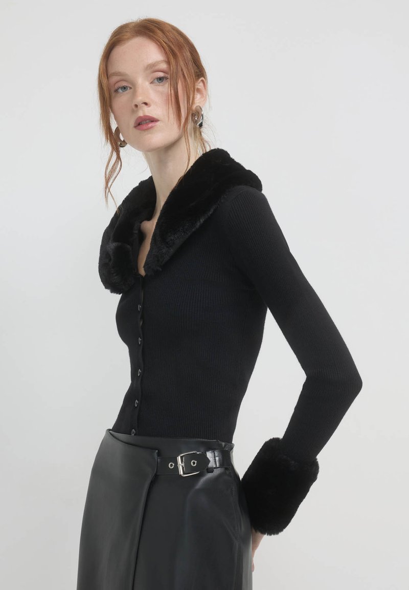 Schwarze gerippte Langarm-Cardigan mit einem flauschigen schwarzen Pelzkragen und -ärmeln. Verfügt über eine durchgehende Knopfleiste und einen glatten Lederrock.