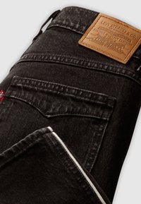 Jean noir Levi's plié, montrant la poche arrière, la passoire de ceinture et l'étiquette de marque en cuir marron cousue sur la ceinture.