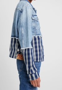 Kurtka z dżinsu i w kratę, z jasnoniebieskim, wyblakłym górnym fragmentem z dżinsu oraz granatowym, kratowanym dolnym fragmentem, z postrzępionymi krawędziami i metką z logo.