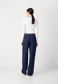 Pantaloni larghi blu navy con una texture liscia, caratterizzati da una vita rossa a contrasto e due tasche posteriori. Abbinati a una maglietta bianca a maniche lunghe.