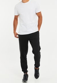 Witte katoenen t-shirt gecombineerd met zwarte joggingbroek. De joggingbroek heeft een taille met trekkoord en bijgesneden enkels. Zwarte sneakers maken de outfit af.