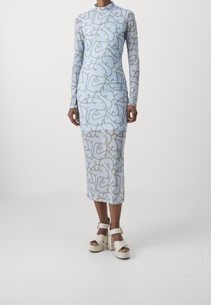 Femme portant une robe bleu clair à manches longues et longueur cheville avec un motif chaîne et cadenas et des sandales à plateforme blanches à talons hauts.
