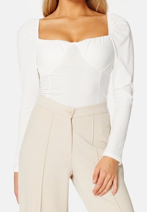 Body bianco a costine con scollatura quadrata e maniche lunghe, abbinato a pantaloni beige a vita alta con dettaglio a bottoni.