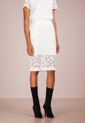 Falda blanca de encaje hasta la rodilla con dobladillo en forma de ondas, combinada con blusa de encaje a juego y botines negros acanalados de tacón alto.
