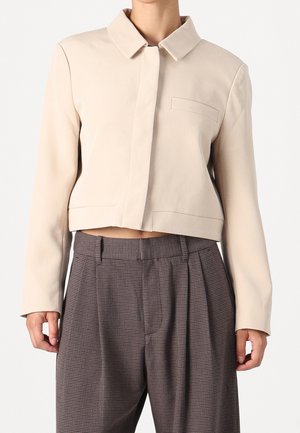 Beige gekürzte Jacke mit verdeckten Knöpfen, Reverskragen und Brusttasche kombiniert mit hoch taillierter grauer karierter plissierter Hose.