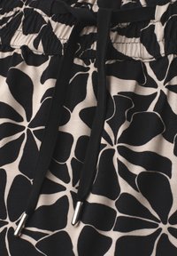 Gros plan d’un tissu à motif floral noir et beige avec une ceinture élastique et un cordon noir noué au centre.