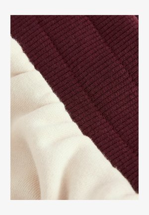 Knit sweater fragment featuring a maroon textured ribbed section and a smooth cream section, highlighting contrasting materials and colors.