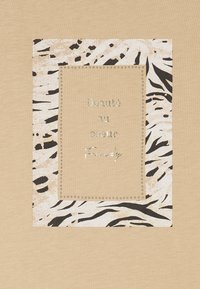 T-shirt beige con una stampa quadrata a motivo zebra e testo metallico che recita "Beauté au cœur Freddy." Bordato con dettagli in borchie.