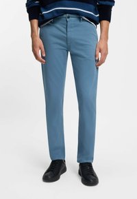 Světle modré bavlněné kalhoty slim fit, se zapínáním na knoflík, předními kapsami a nošeny s černými teniskami.