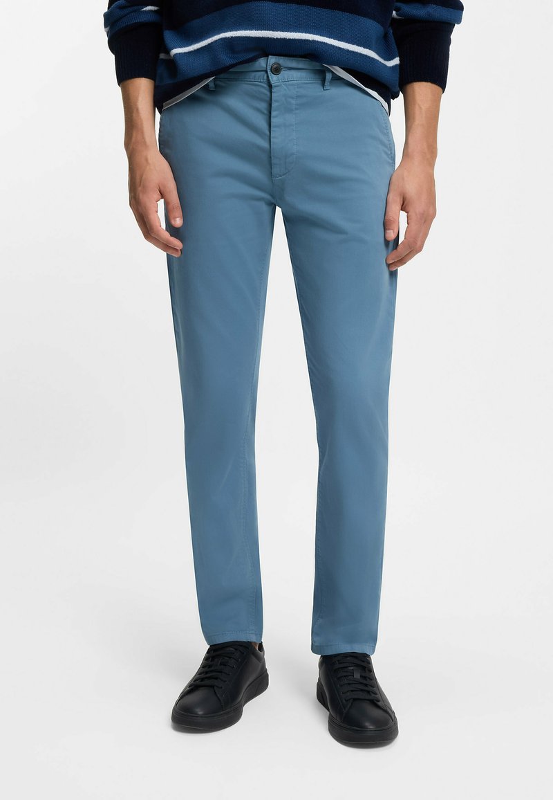 Světle modré bavlněné kalhoty slim fit, se zapínáním na knoflík, předními kapsami a nošeny s černými teniskami.