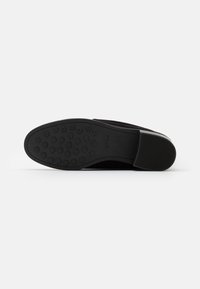 Semelle de chaussure noire avec un motif texturé, comportant des grips circulaires et une bordure lisse. Fabriquée en caoutchouc avec une forme profilée.