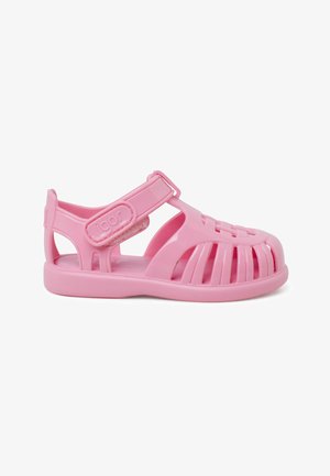 Roza plastična sandal s odprtim dizajnom, ki ima Velcro trak, ravno podplato in izrezljane detajle na zgornjem delu za dobro prezračevanje.