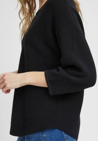 Schwarzer Strickpullover mit strukturiertem Oberflächen, drei Viertelärmeln, einem weitem Kragen und einem leicht verlängerten hinteren Saum.