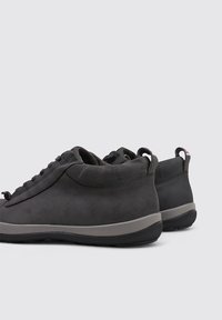 Zapatillas de ante negro con forma curvada, diseño minimalista, acentos en gris y suelas de goma. Cuentan con una lengüeta en el talón.