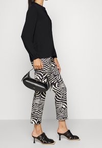 Blouse noire à manches longues, pantalon à motifs zèbre noir et blanc, sac à main noir texturé, et mules noires à talons ouvertes.